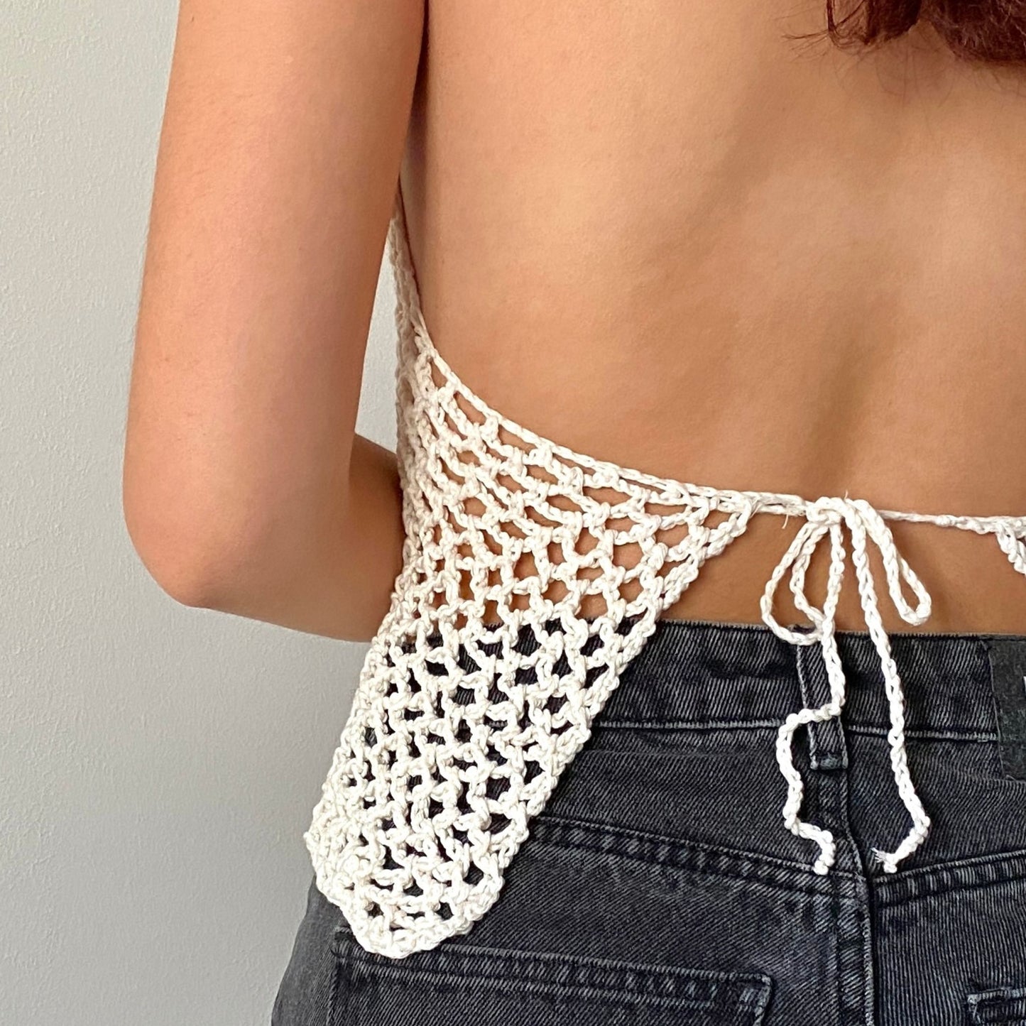 Pige poserer i en hvid hæklet halter top med gennemsigtige mesh paneler med ryggen vendt mod kameraet