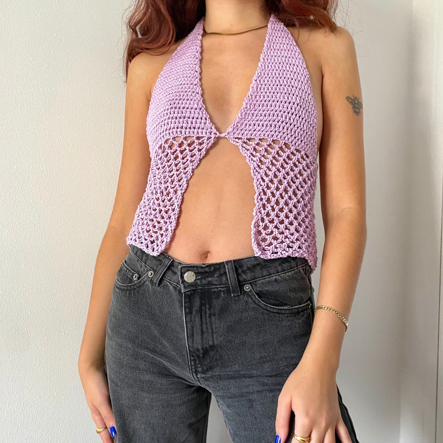Pige poserer i en lyselilla hæklet halter top med gennemsigtige mesh paneler og en sløjfe foran