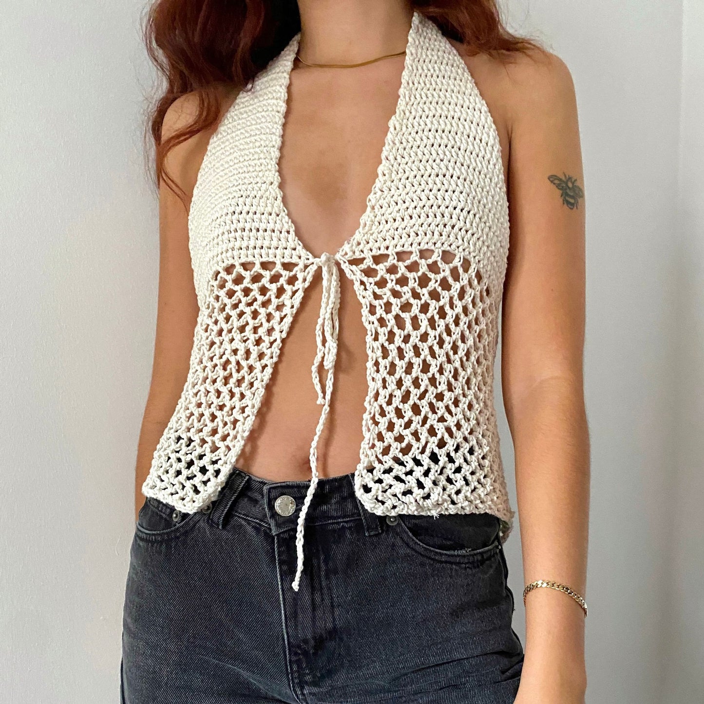 Girl posing in a white halter neck crochet top with see-through mesh panels and a bow in the front