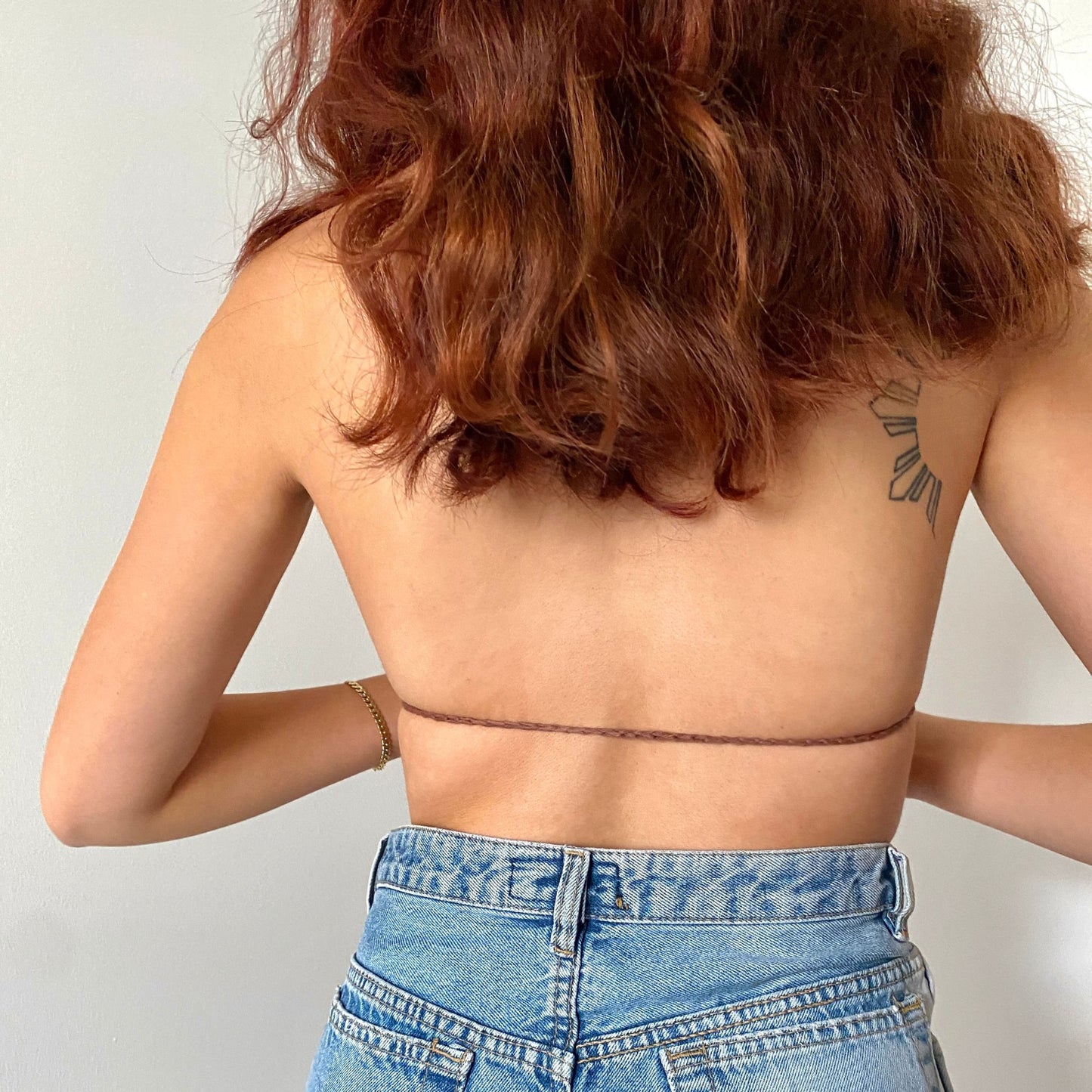 Girl posing in a brown, beige and white striped crochet triangle bikini top that ties around the neck shown from the back